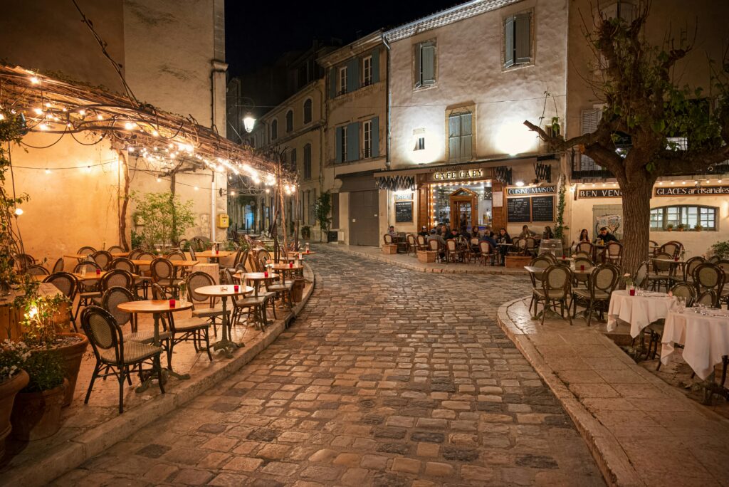 Rue pavée et café animé à Lourmarin de nuit, ambiance chaleureuse d’un village de Provence. Night scene in Lourmarin with cobbled streets and lively cafés, warm Provençal atmosphere.